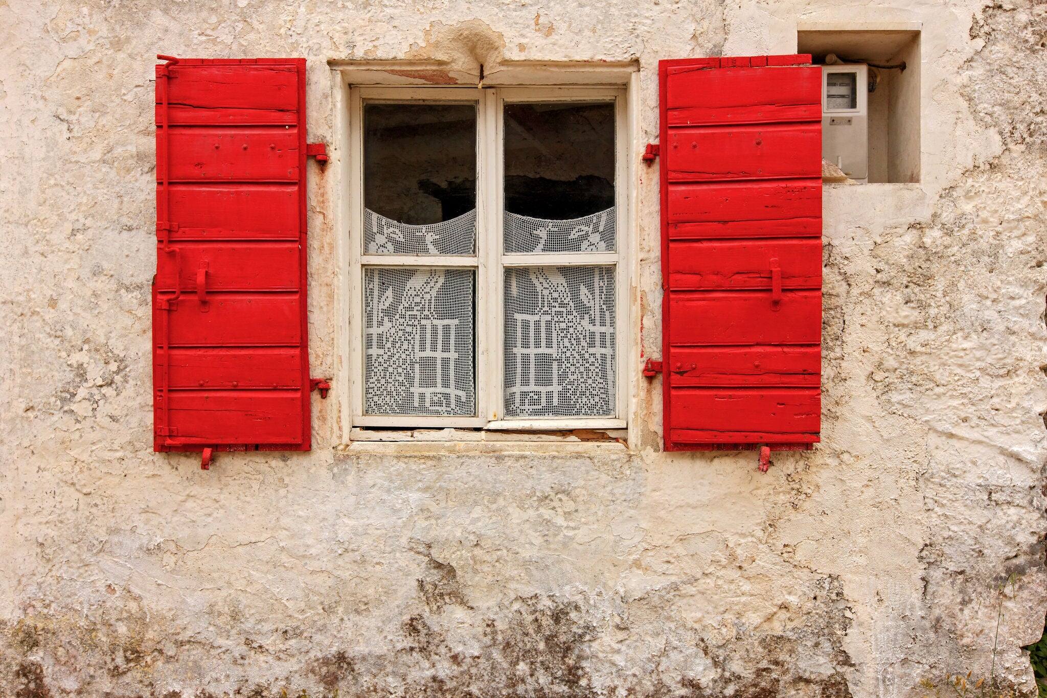 Picturesque facade of traditional local house with stone wall, red window and elaborate lace as curtains, seen in a village of Zakynthos island, Ionian Sea, Greece, Europe.