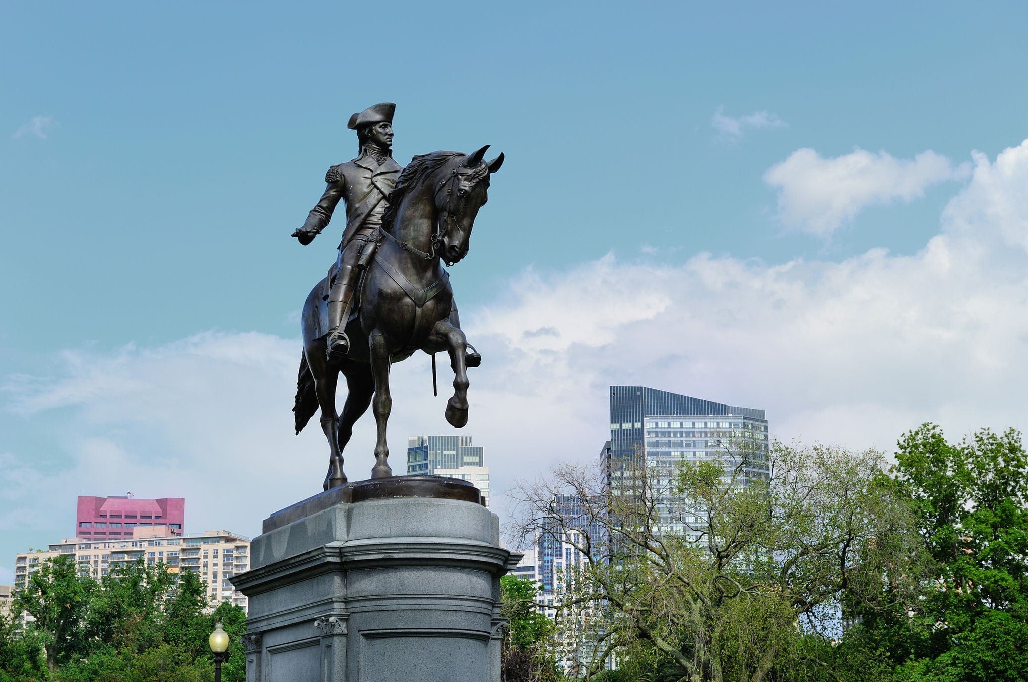 George Washington statue as the famous landmark in Boston Common Park with city skyline and skyscrapers.