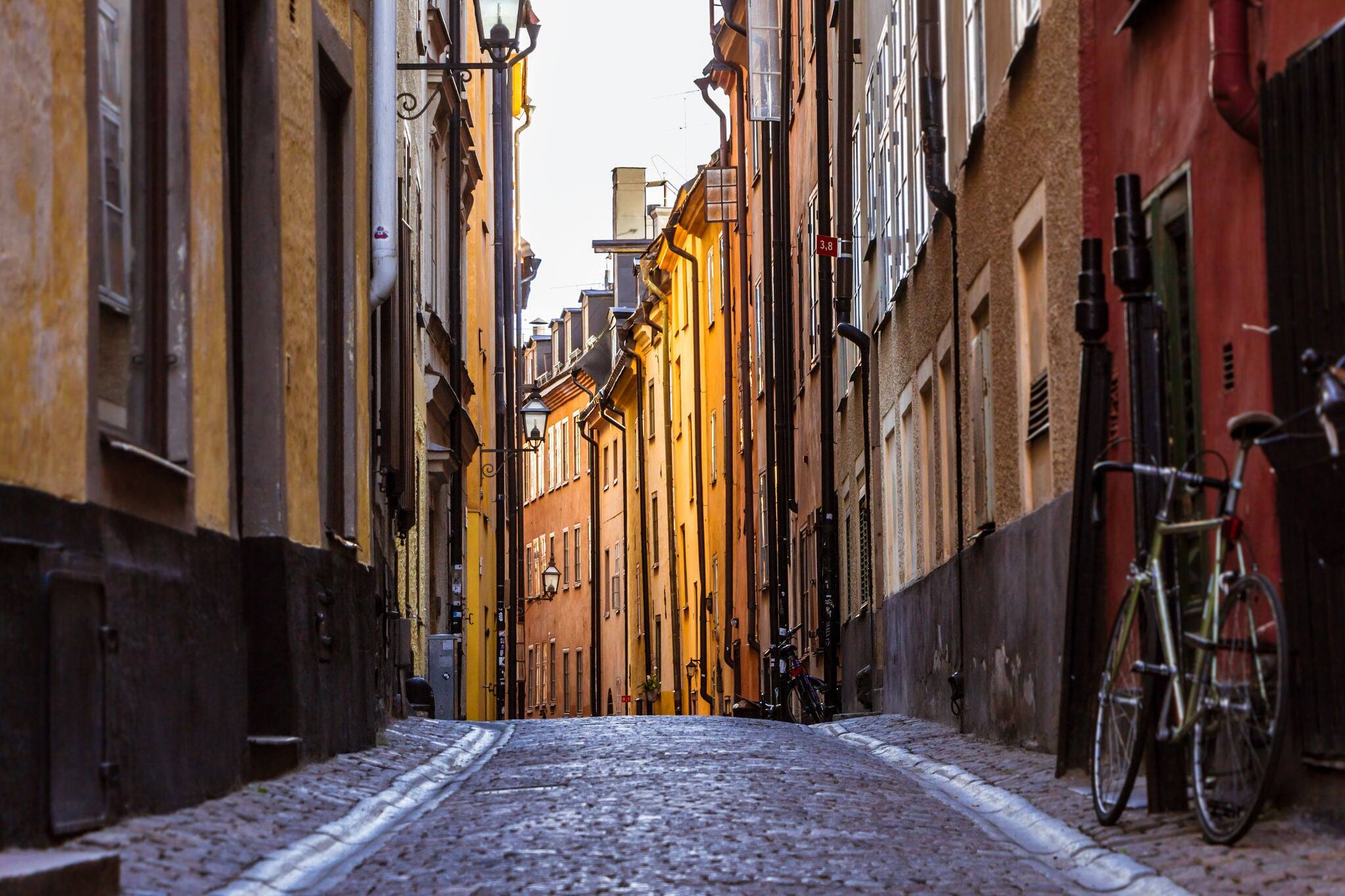 Gamla Stan. Stockholm, Sweden. Colorful Cobbled street in Old Town. Color street with cobblestone road, orange houses, streetlight and bicycle. Perspective of the Narrow  street. Focus in the center.