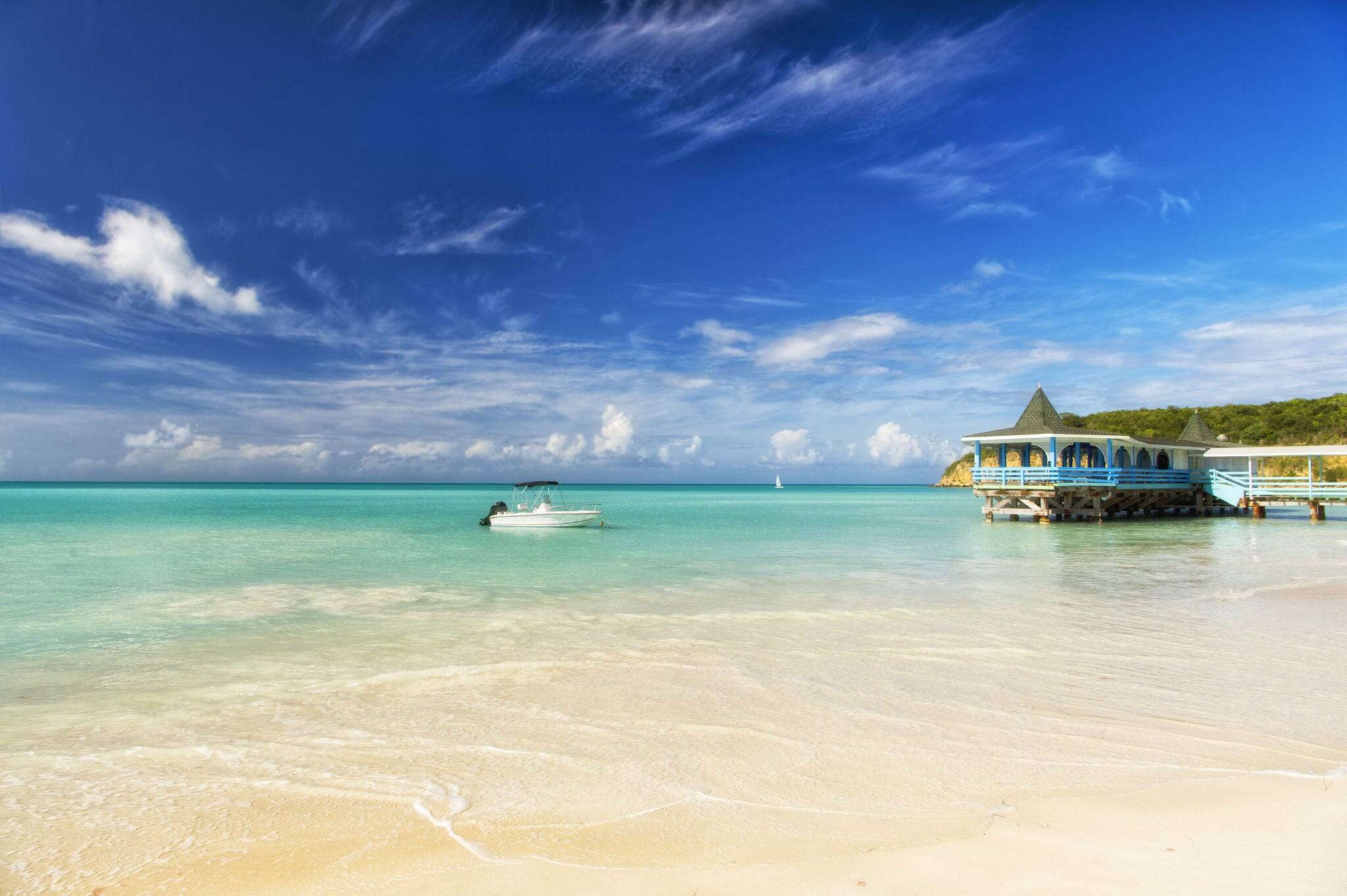 Exotic beautiful marine beach of Antigua St. Johns with one wave runner on water and house with small clouds in sunny sky outdoor on natural background