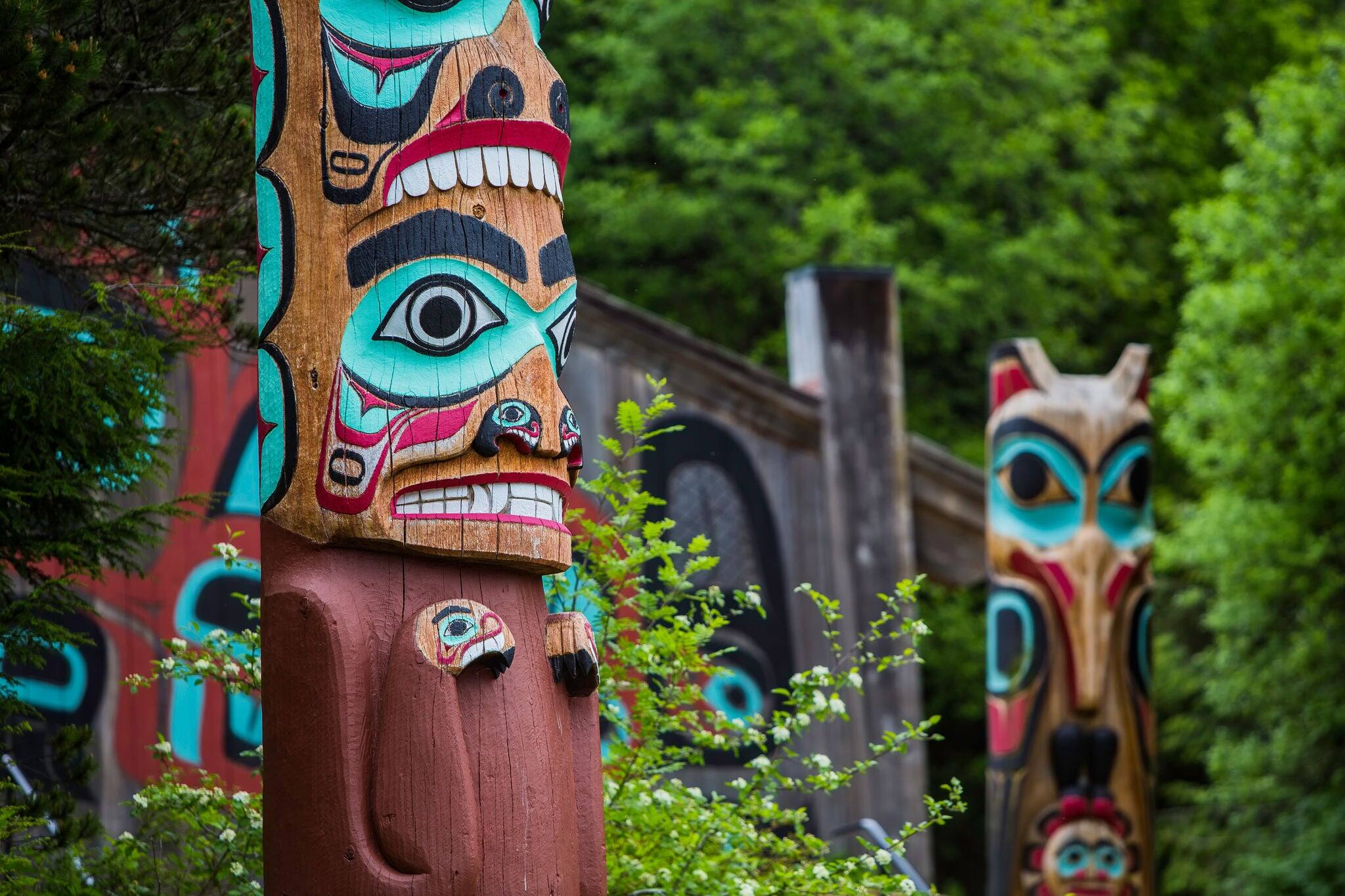 Detail of totem pole at Saxman Village tribal house near Ketchikan Alaska with Sun Raven in background