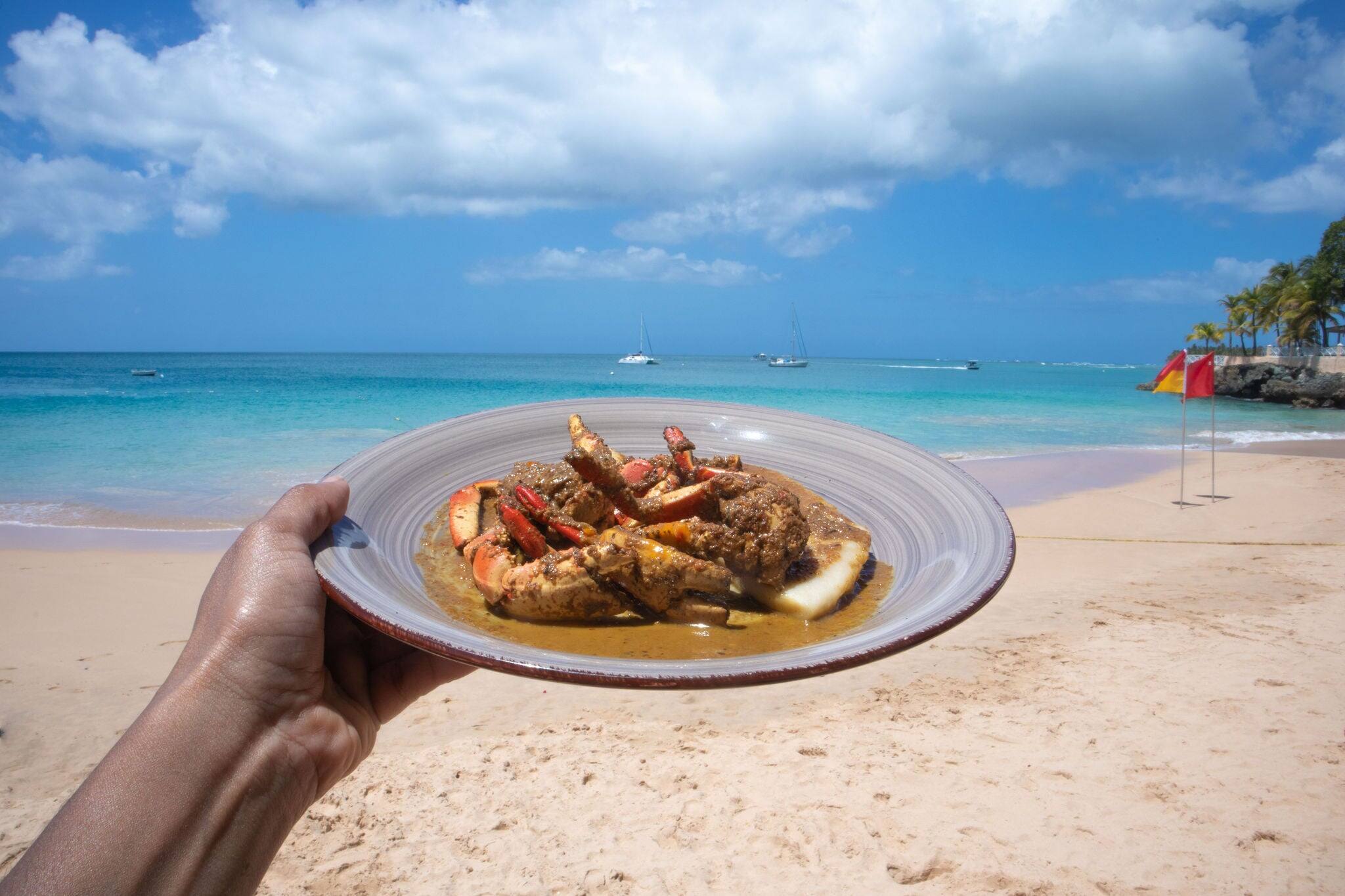 Curry crab and dumpling on a plate, hand held while enjoying the view of Store Bay, Tobago, Trinidad and Tobago