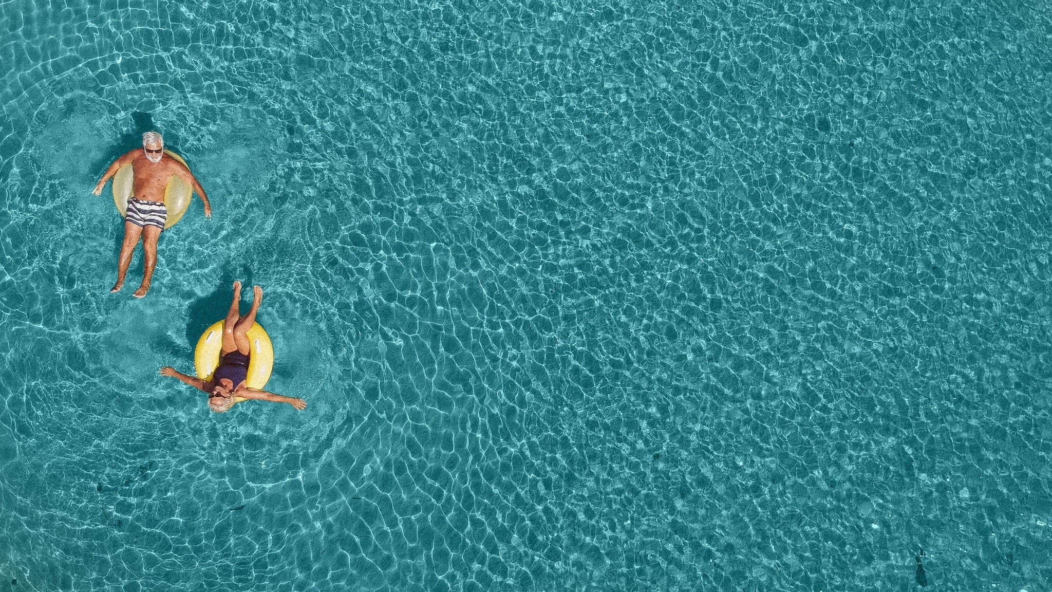 High angle view photo of a senior couple floating in the ocean while using swimming and floating devices; wide photo dimensions