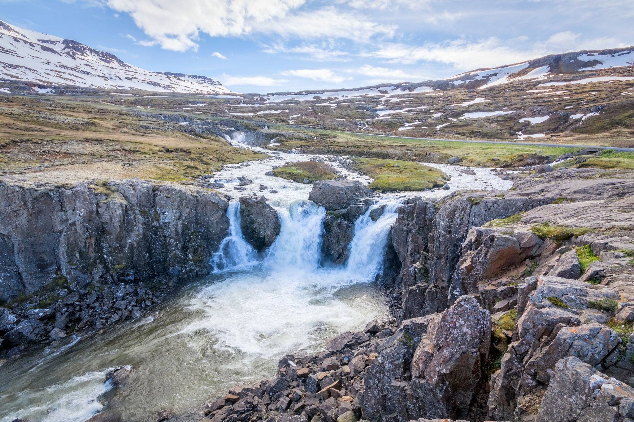 Landscape with waterfall, snowy mountain tops with blue sky.  Seydisfjordur, Iceland.