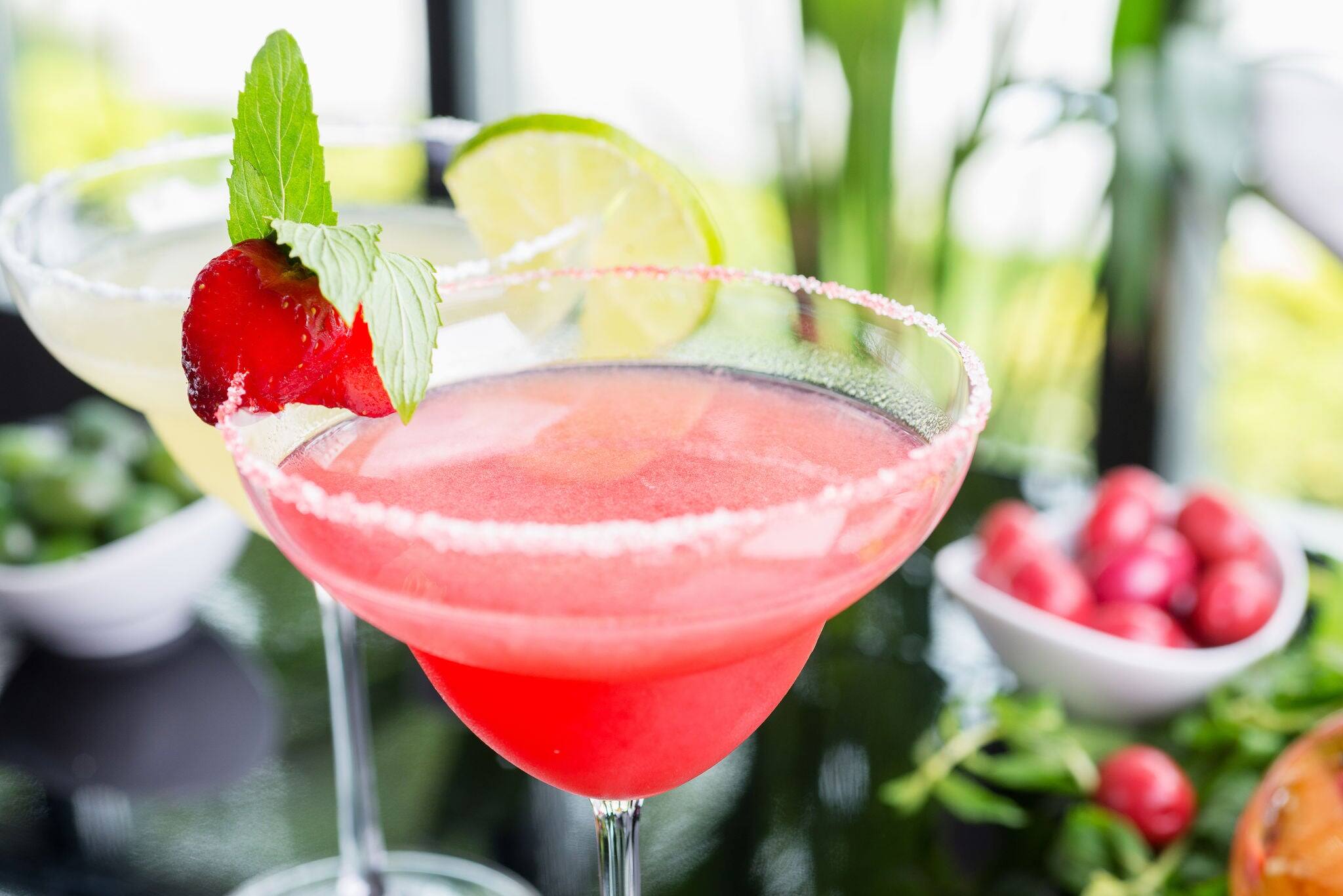 mix of the bright refreshing cocktails lime and strawberry daiquiri on a table in a restaurant with decoration of salt on the edge of the glass with fresh mint and lime slices and berries. soft focus