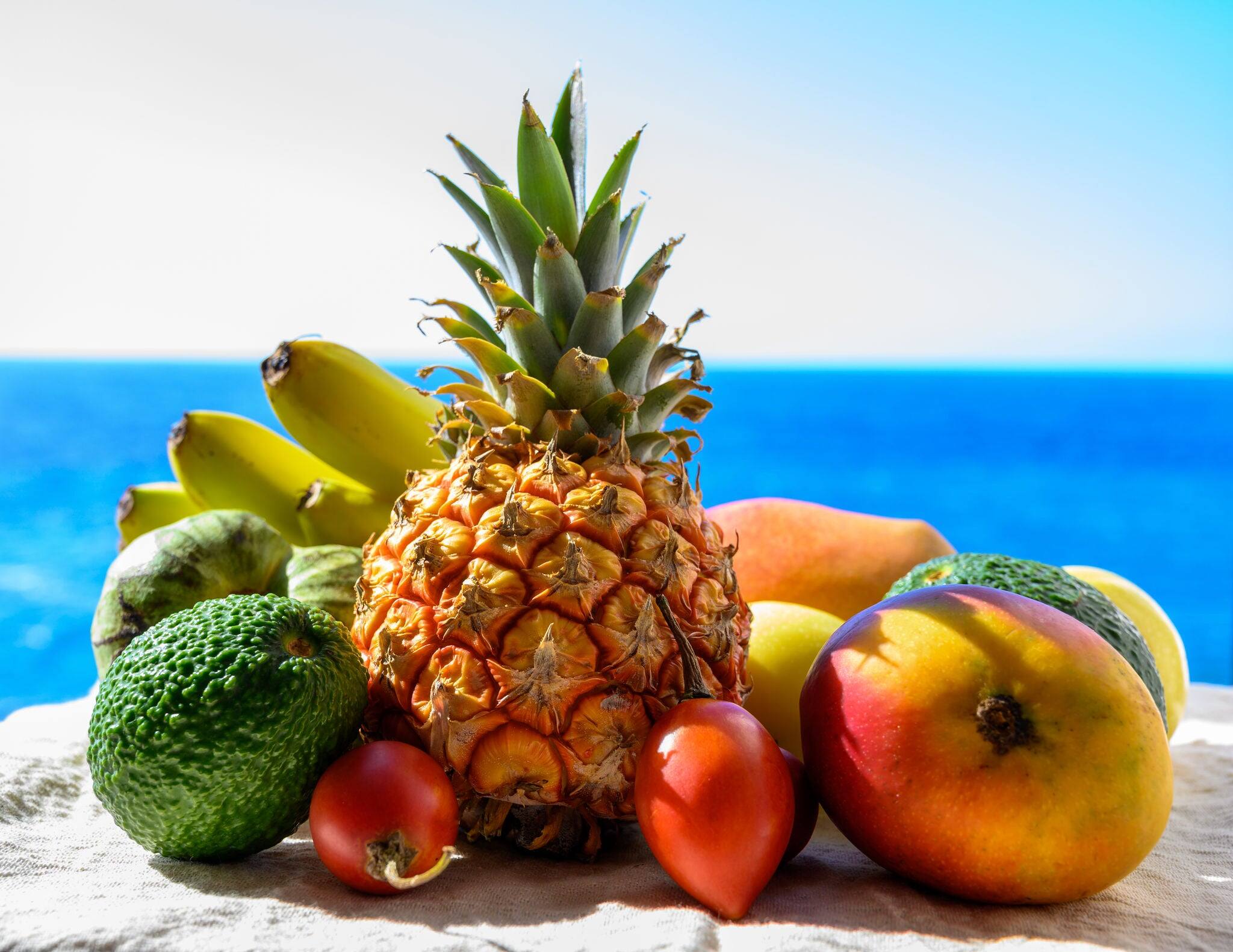 Tropical fruits collection, custard apple or green ripe cherymoia, passion fruit, pineapple, mango, tamarillo, avocado exotic fruits on blue sea background in sunny day