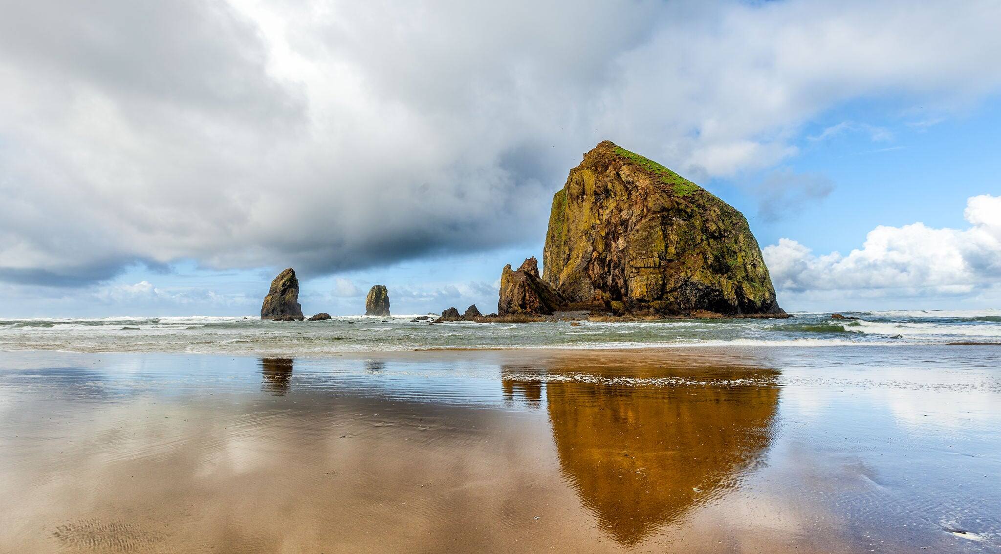 Oregon coast scenic Haystack Rock on a dramatic day with clouds and reflections. Famous destination for bird watchers.
