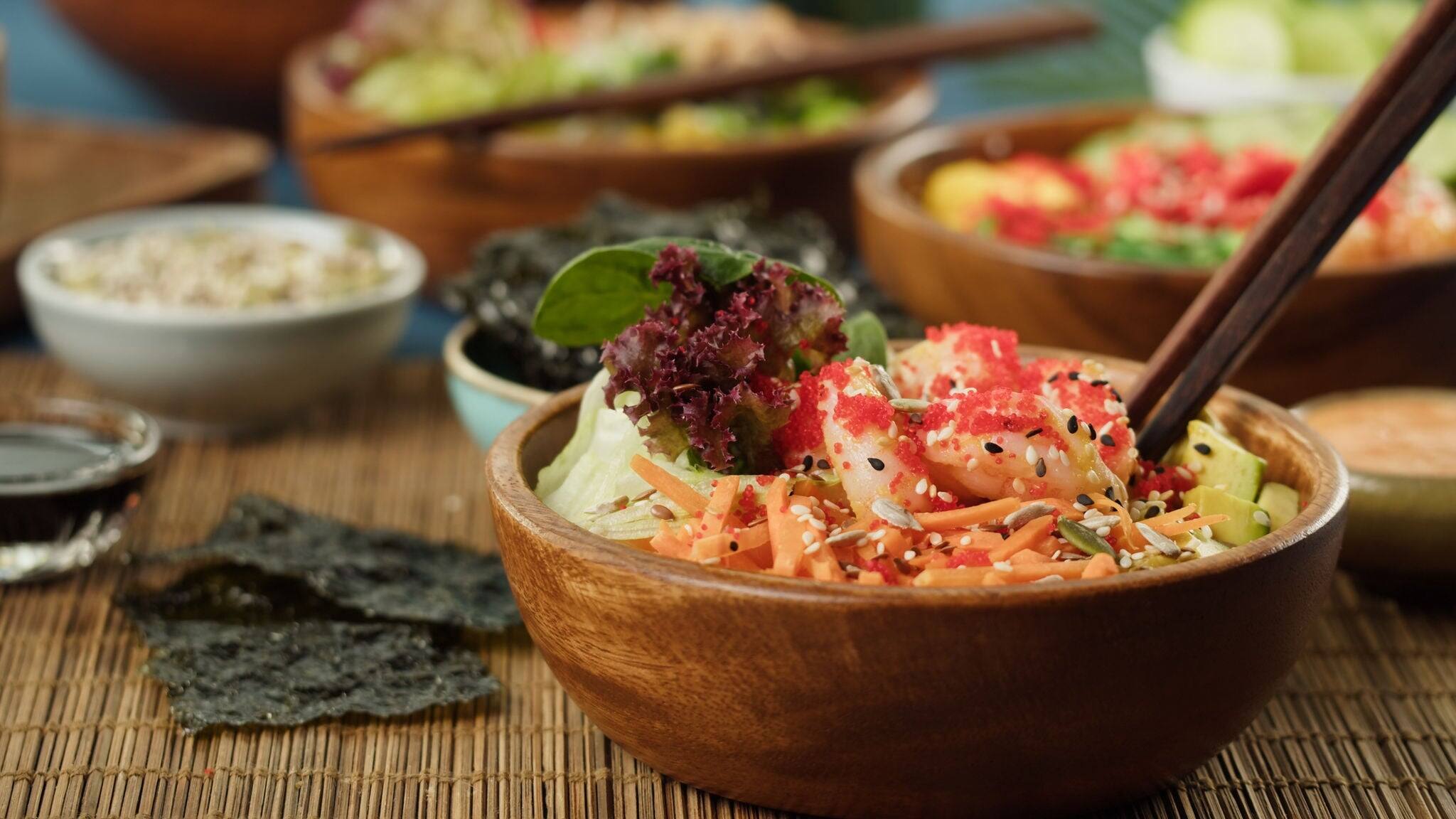Traditional Hawaiian cuisine on table close-up. Cooked poke bowls served with sliced vegetables, fish and greenery, dried seaweed. Healthy vegetarian food. Asian vegan raw meal, chopsticks.