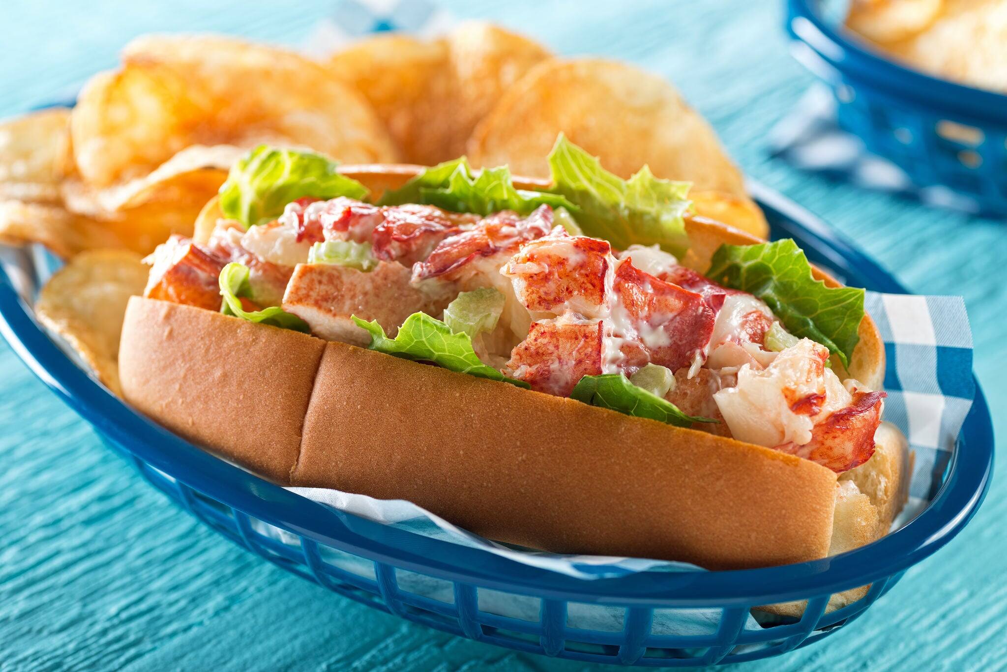 A delicious lobster roll with lettuce, celery, mayonnaise, and potato chips.