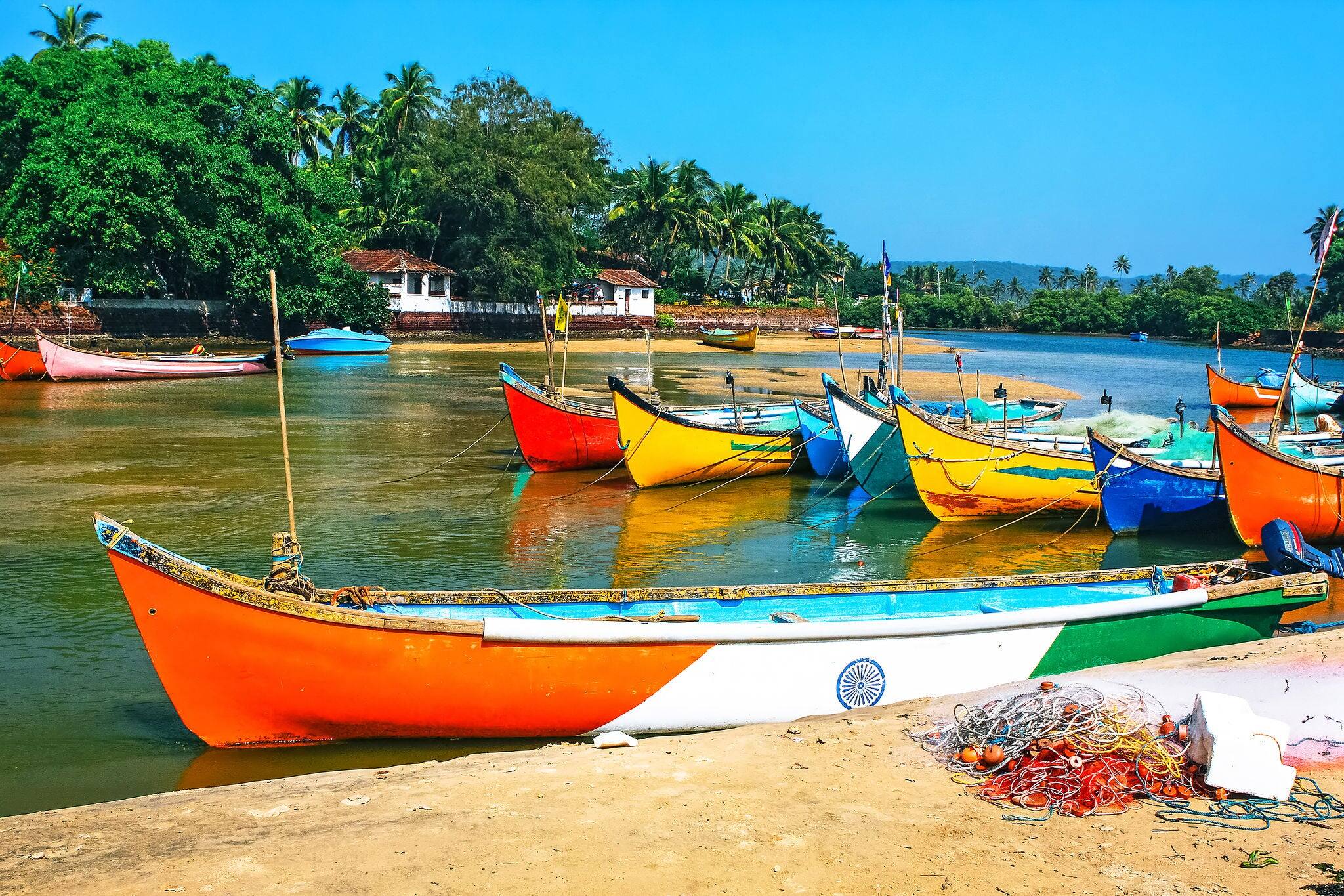 fishing boats on the beach  in tropical with palms, huts and blue sky. Goa, India