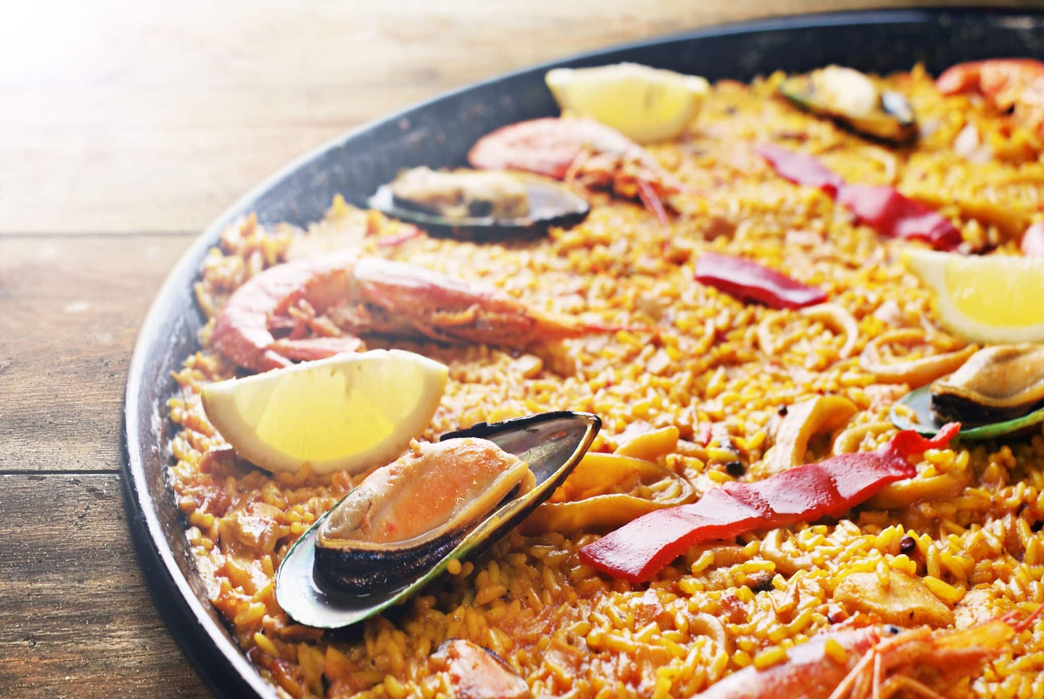 Spanish seafood paella in traditional pan on wooden planks.