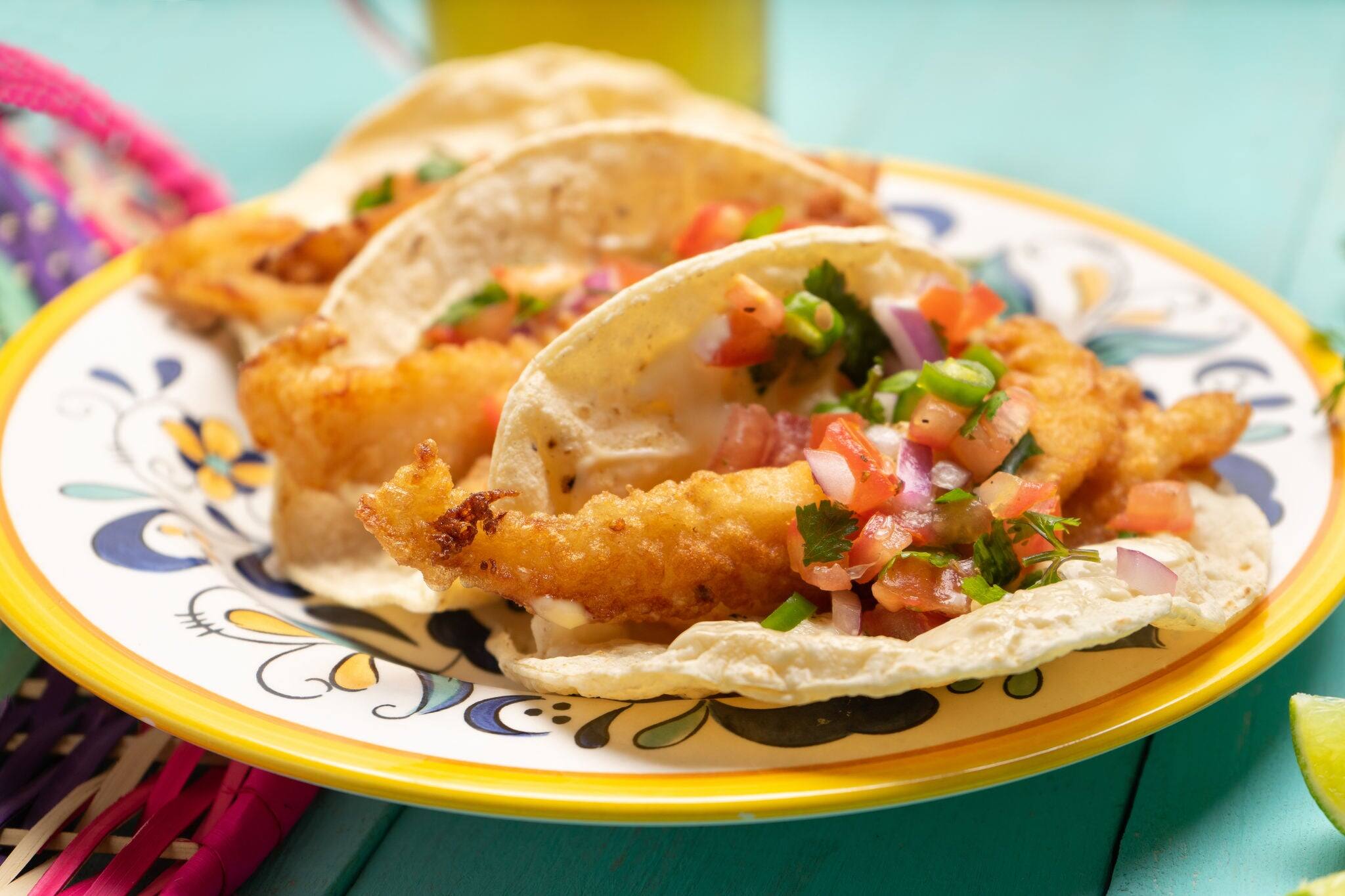 Traditional mexican breaded fish tacos also called ensenada on turquoise background