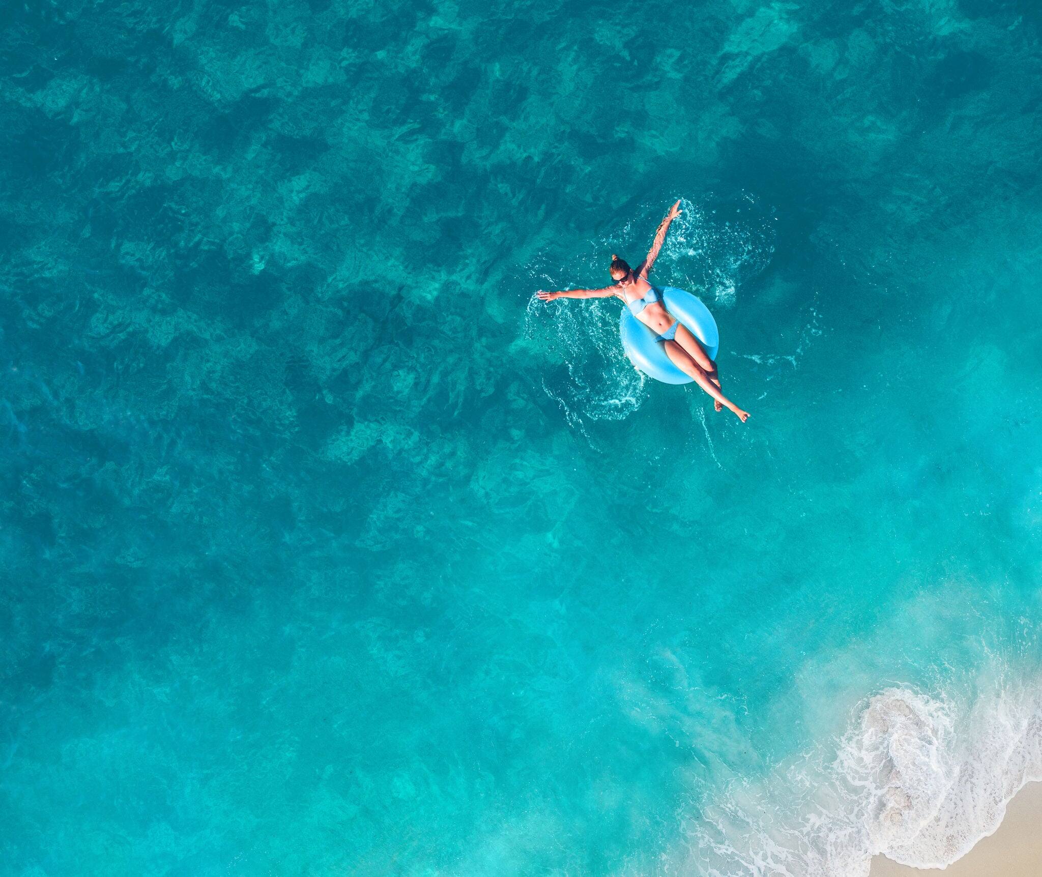 High angle view photo of a young woman relaxing while floating in the ocean using swimming tube; wide photo dimensions
